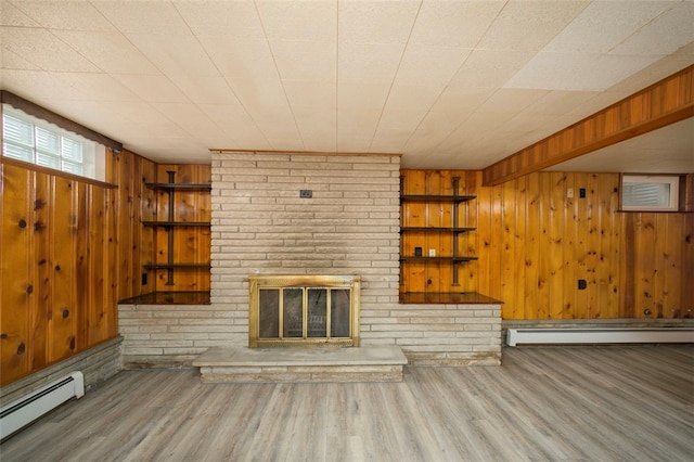 unfurnished living room featuring wood-type flooring, wooden walls, a fireplace, and a baseboard heating unit