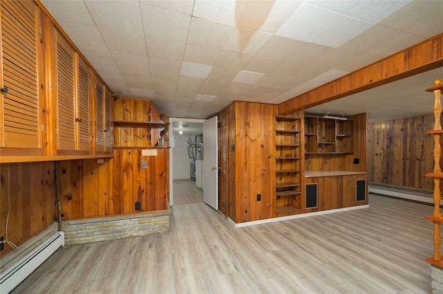 basement featuring wood walls, a baseboard heating unit, and light hardwood / wood-style flooring