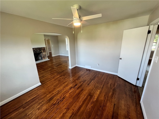 empty room with ceiling fan, dark hardwood / wood-style flooring, and a fireplace