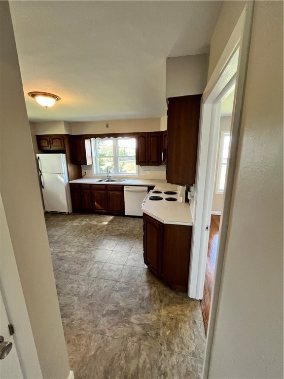 kitchen with white appliances, dark brown cabinetry, and sink