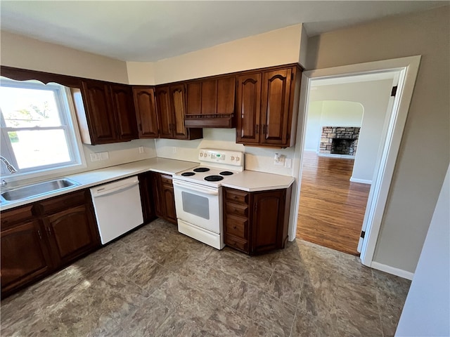 kitchen with light hardwood / wood-style flooring, a stone fireplace, dark brown cabinetry, sink, and white appliances