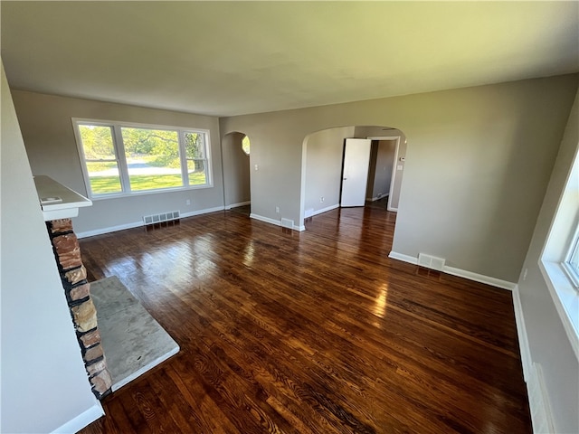 unfurnished living room with a stone fireplace and dark hardwood / wood-style floors