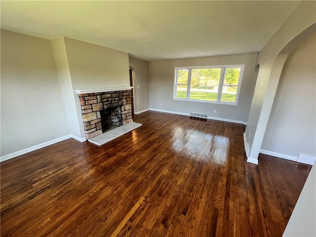 unfurnished living room featuring dark wood-type flooring and a stone fireplace