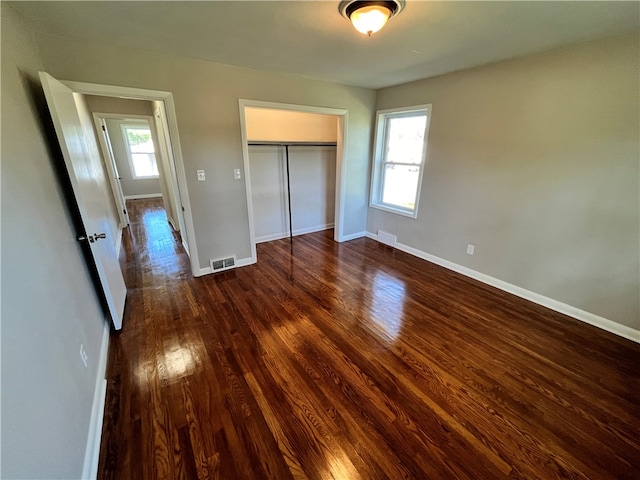 unfurnished bedroom with a closet, multiple windows, and dark hardwood / wood-style flooring