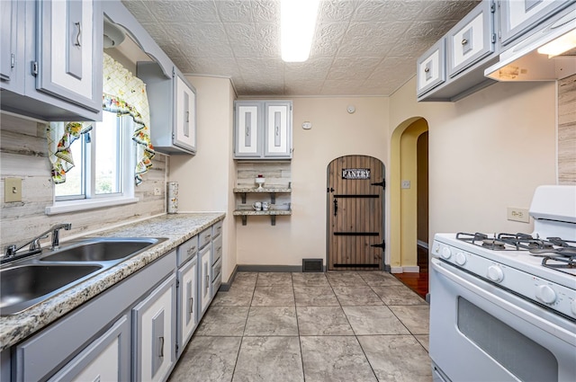 kitchen featuring white gas range, backsplash, sink, and white cabinets