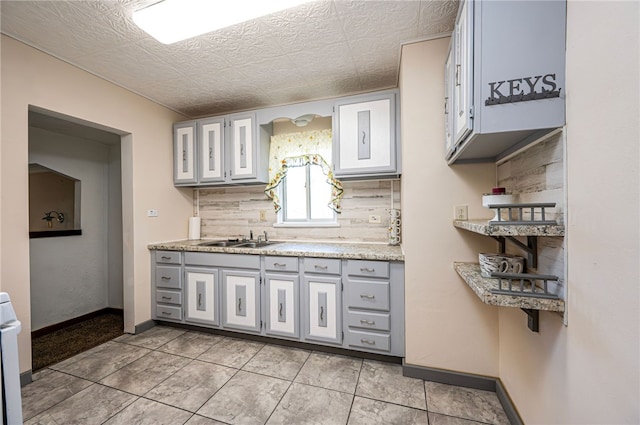 kitchen featuring tasteful backsplash, light tile patterned floors, range, gray cabinetry, and sink