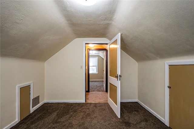 additional living space featuring dark carpet, vaulted ceiling, and a textured ceiling