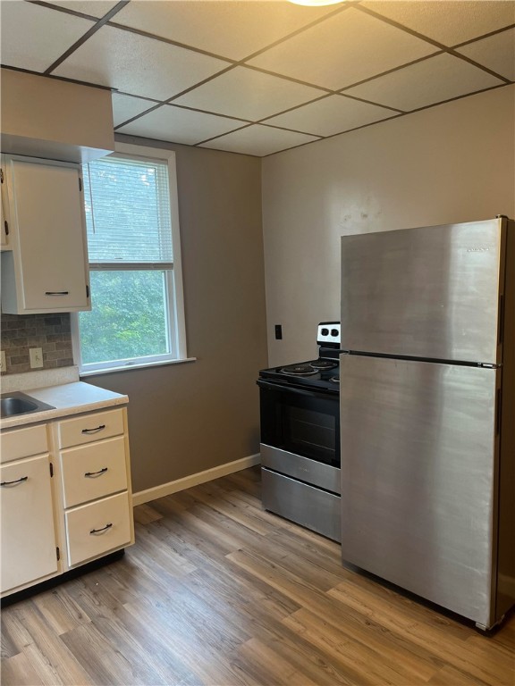 kitchen with backsplash, white cabinetry, stainless steel appliances, a drop ceiling, and light wood-type flooring