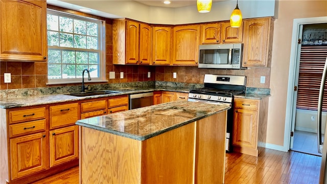 kitchen with light hardwood / wood-style floors, decorative light fixtures, sink, appliances with stainless steel finishes, and a center island