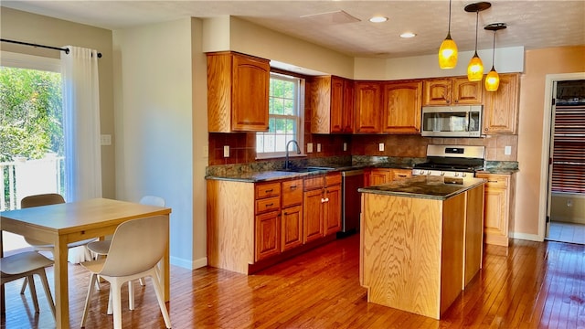 kitchen featuring wood-type flooring, decorative light fixtures, sink, appliances with stainless steel finishes, and a center island