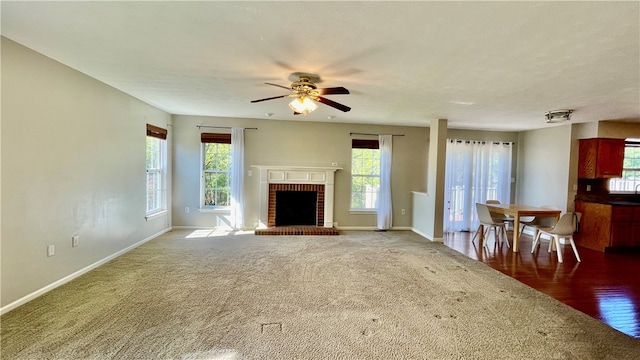 unfurnished living room featuring wood-type flooring, a brick fireplace, plenty of natural light, and ceiling fan