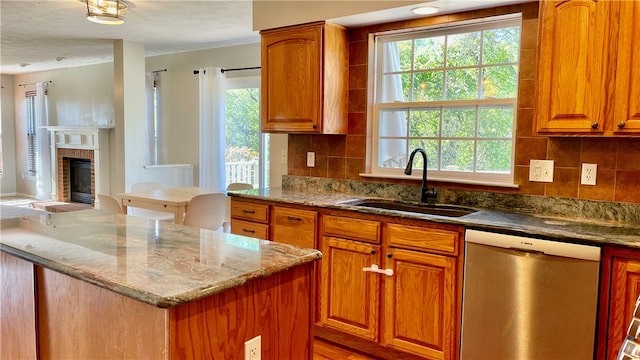 kitchen with a brick fireplace, sink, dishwasher, light stone countertops, and backsplash