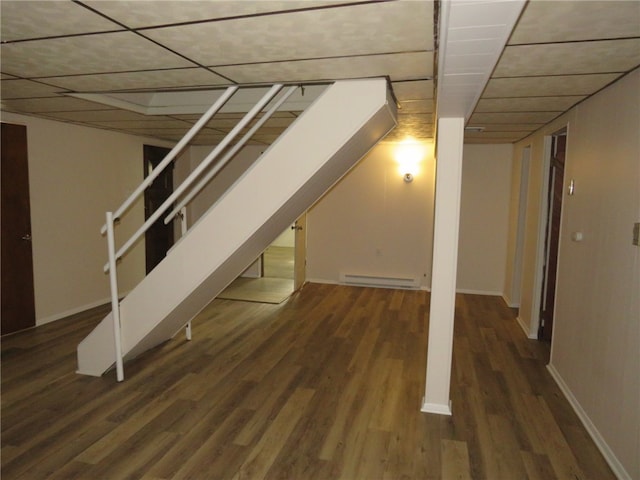 basement with a paneled ceiling, dark wood-type flooring, and a baseboard heating unit