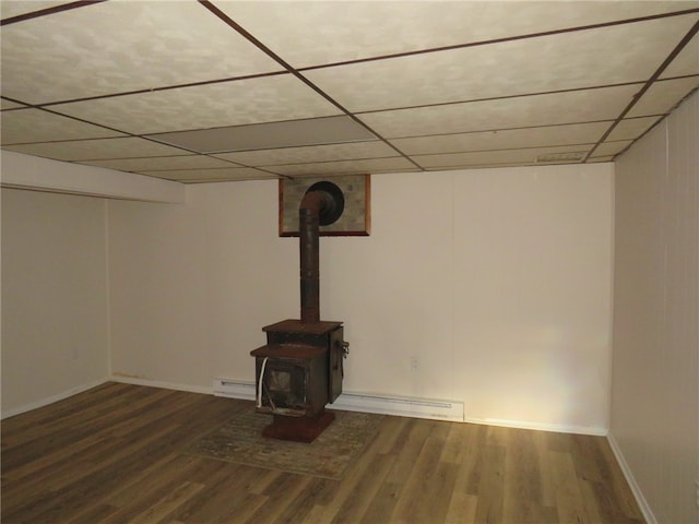 basement featuring a baseboard heating unit, a paneled ceiling, hardwood / wood-style floors, and a wood stove