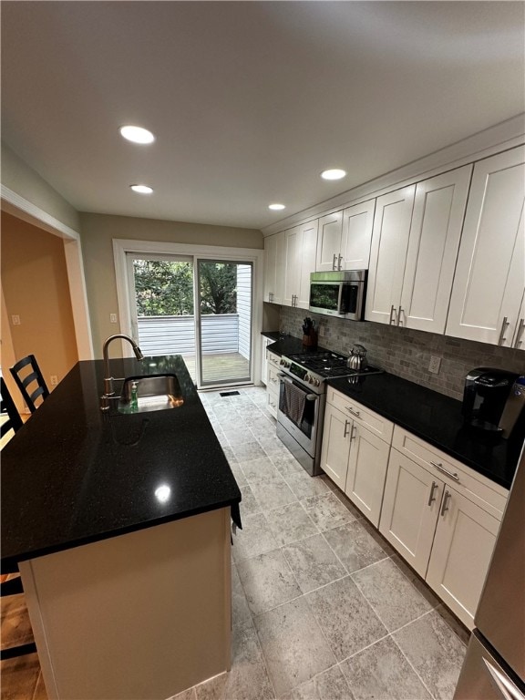 kitchen featuring sink, a center island with sink, backsplash, white cabinetry, and stainless steel appliances