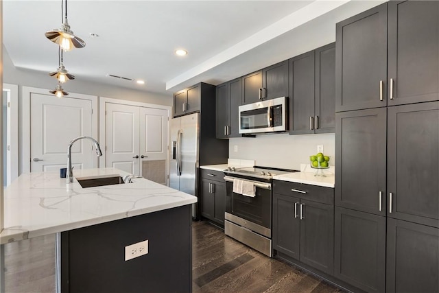 kitchen featuring light stone counters, dark wood-type flooring, a kitchen island with sink, stainless steel appliances, and a sink