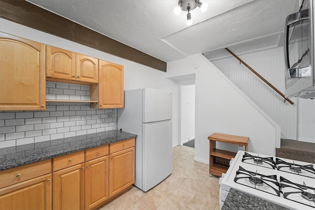 kitchen with tasteful backsplash, white appliances, dark stone counters, light tile patterned floors, and a textured ceiling