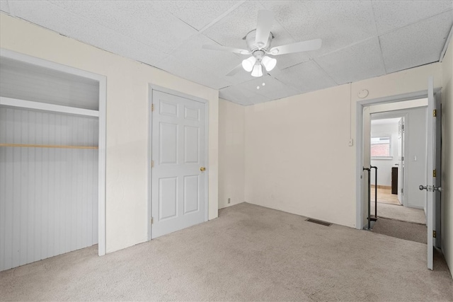 unfurnished bedroom with wood walls, a closet, ceiling fan, and light carpet