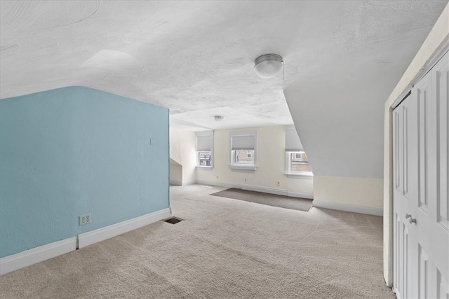 bonus room featuring vaulted ceiling, a textured ceiling, and light carpet