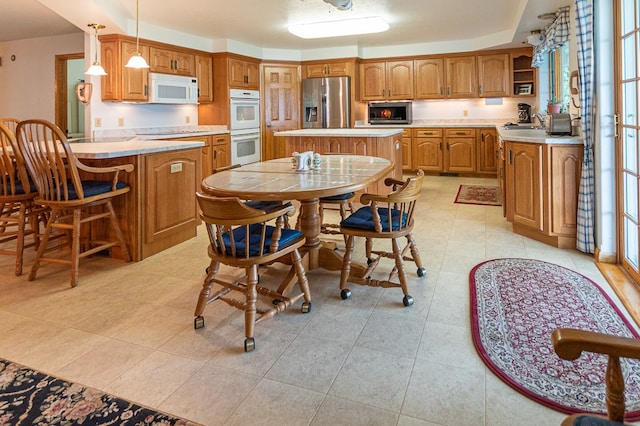 kitchen featuring a kitchen island, sink, light tile patterned flooring, appliances with stainless steel finishes, and decorative light fixtures