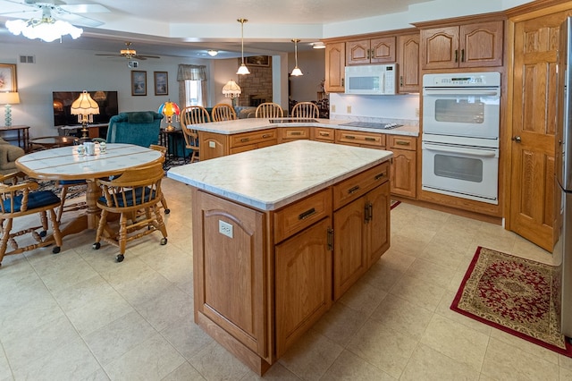 kitchen with a brick fireplace, ceiling fan, pendant lighting, white appliances, and a kitchen island