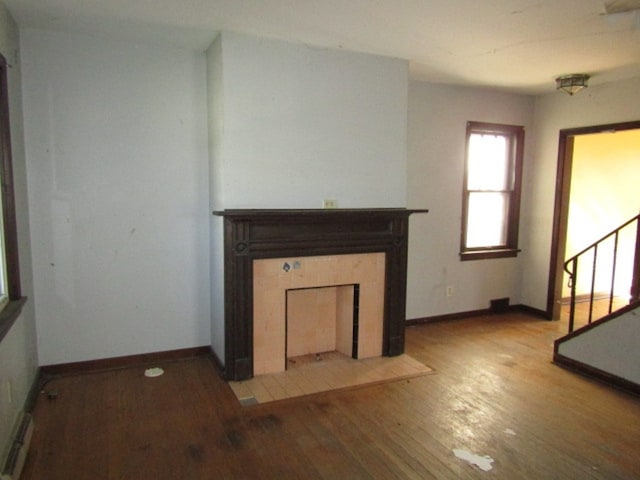 unfurnished living room featuring wood-type flooring and a tiled fireplace