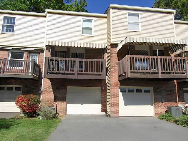 rear view of house with a garage, driveway, brick siding, and cooling unit