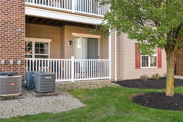 view of exterior entry featuring central air condition unit, a balcony, and a lawn