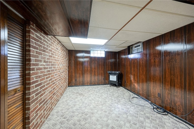 basement with light carpet, a drop ceiling, wood walls, and brick wall