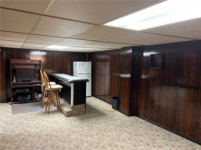 interior space with dark brown cabinets, a paneled ceiling, wooden walls, white fridge, and light colored carpet