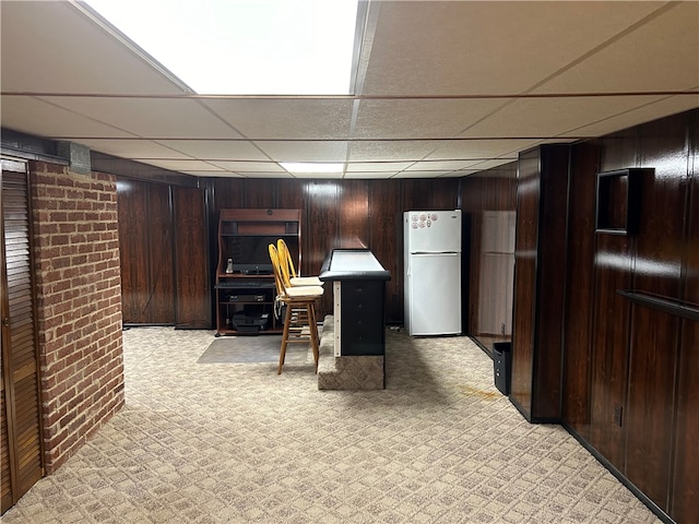 interior space with a drop ceiling, wood walls, light colored carpet, and white refrigerator