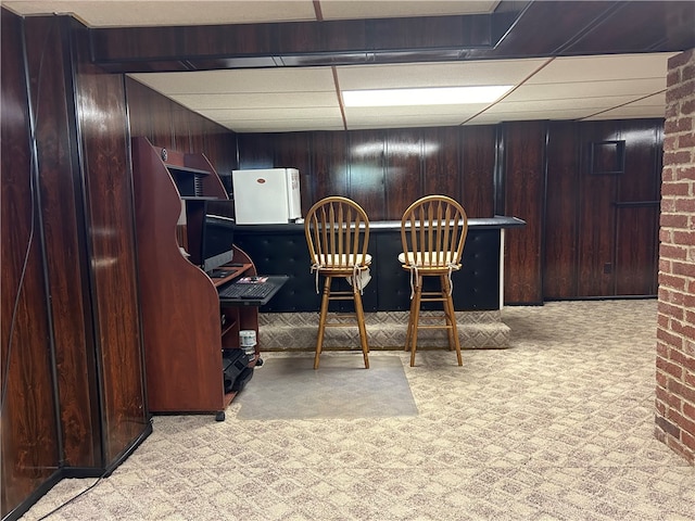 carpeted dining area with a drop ceiling, wood walls, and bar area