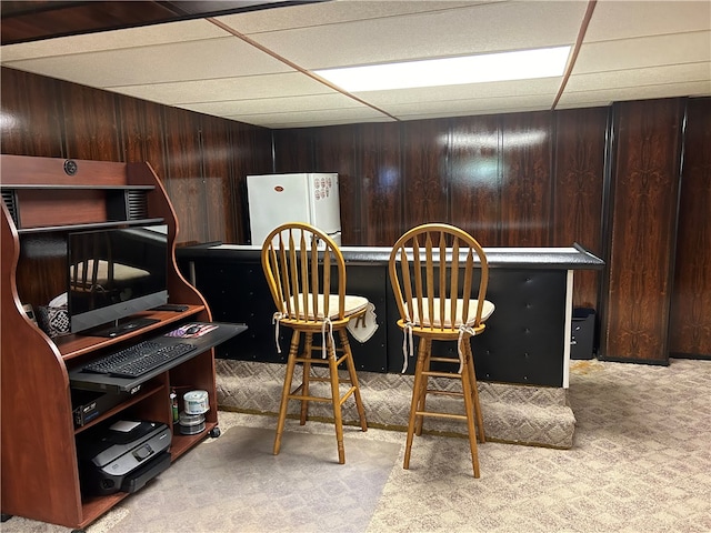 bar featuring carpet floors, dark brown cabinetry, white fridge, a paneled ceiling, and wood walls