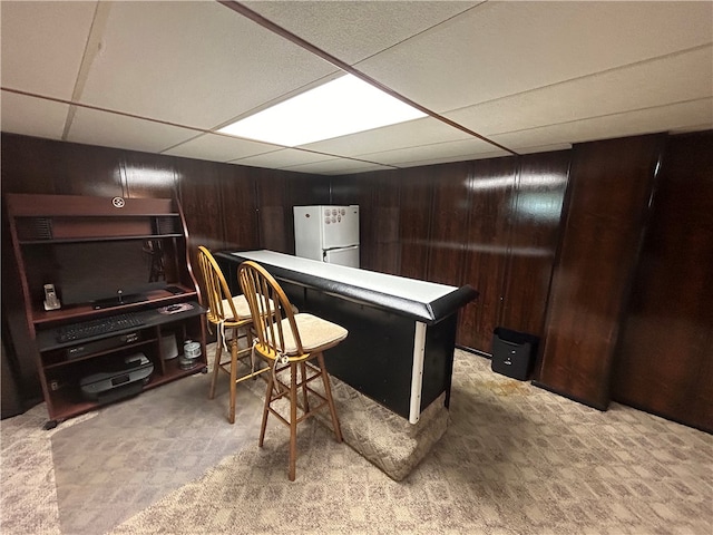 interior space featuring light carpet, white fridge, a paneled ceiling, and wood walls