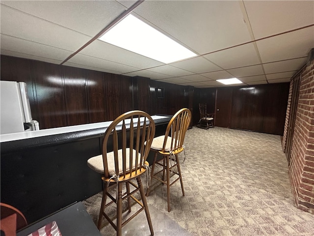 bar featuring light colored carpet, a paneled ceiling, white refrigerator, and wooden walls