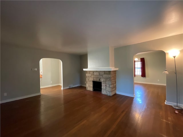 unfurnished living room with a stone fireplace and dark hardwood / wood-style flooring