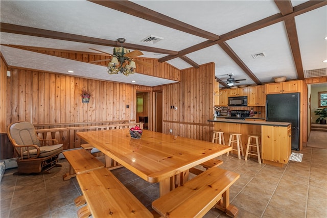 dining room featuring lofted ceiling with beams, ceiling fan, wood walls, and light tile patterned floors