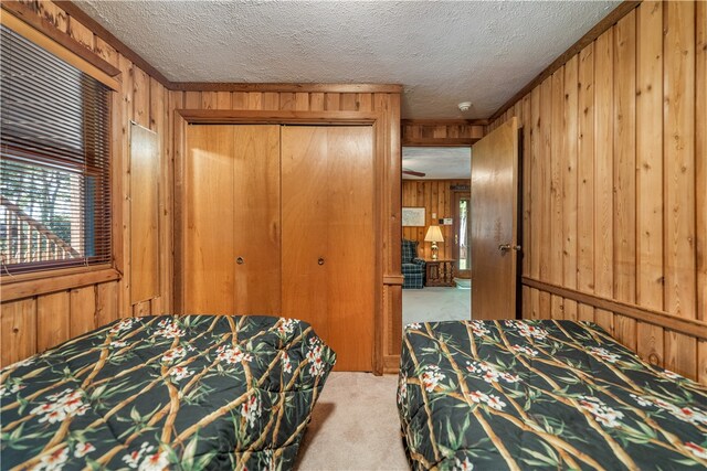 bedroom with a textured ceiling, a closet, wooden walls, and light carpet