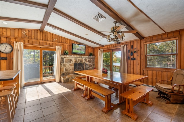 tiled dining area featuring a stone fireplace, a textured ceiling, and wood walls