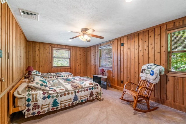 carpeted bedroom with wooden walls, ceiling fan, and a textured ceiling