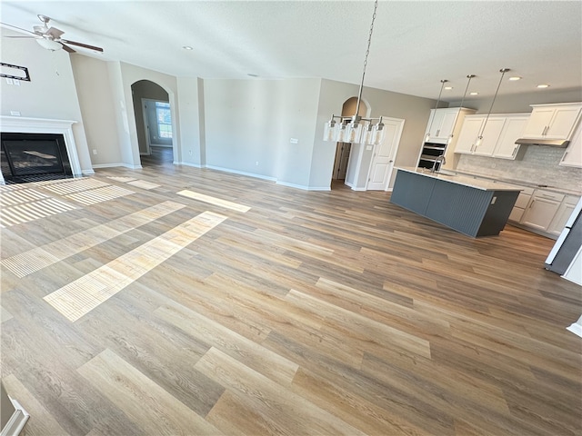 kitchen featuring light wood-type flooring, a kitchen island with sink, tasteful backsplash, hanging light fixtures, and white cabinetry