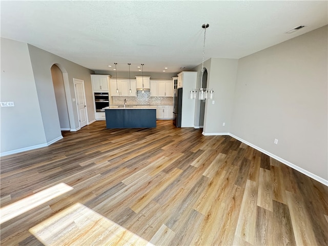 kitchen featuring decorative backsplash, wood-type flooring, a center island with sink, decorative light fixtures, and stainless steel appliances