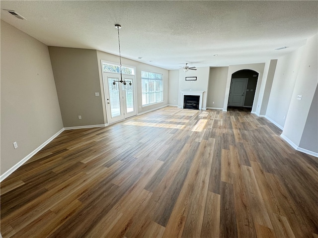 unfurnished living room featuring ceiling fan with notable chandelier, dark hardwood / wood-style flooring, and a textured ceiling