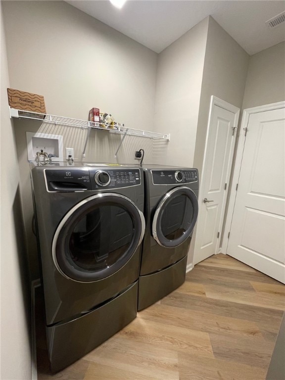 clothes washing area featuring washing machine and clothes dryer and light hardwood / wood-style flooring