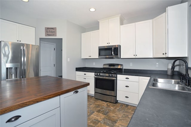 kitchen with stainless steel appliances, butcher block countertops, sink, and white cabinetry