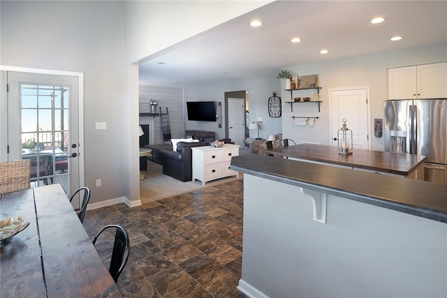 kitchen featuring a breakfast bar area, a fireplace, stainless steel fridge with ice dispenser, and white cabinetry