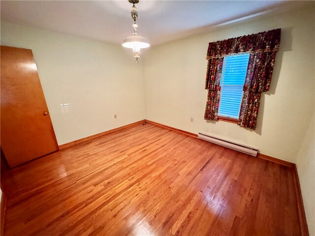 empty room featuring hardwood / wood-style flooring and a baseboard heating unit