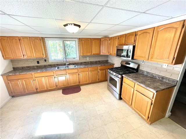 kitchen with decorative backsplash, a paneled ceiling, appliances with stainless steel finishes, and sink