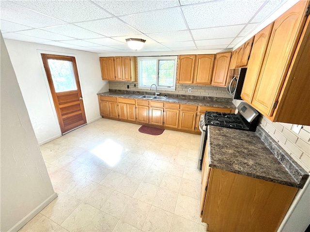 kitchen featuring a drop ceiling, dark stone counters, sink, stainless steel appliances, and backsplash