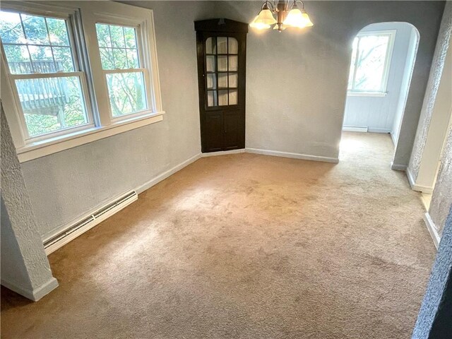 carpeted empty room with an inviting chandelier, a wealth of natural light, and a baseboard radiator